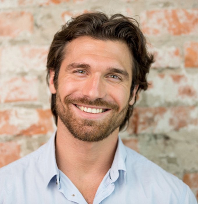 Man standing against a brick wall and smiling