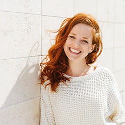 Woman in white sweater leaning against a wall