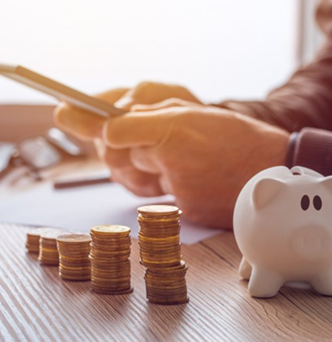 Individual using a calculator at their desk next to a small piggy bank and stacks of coins