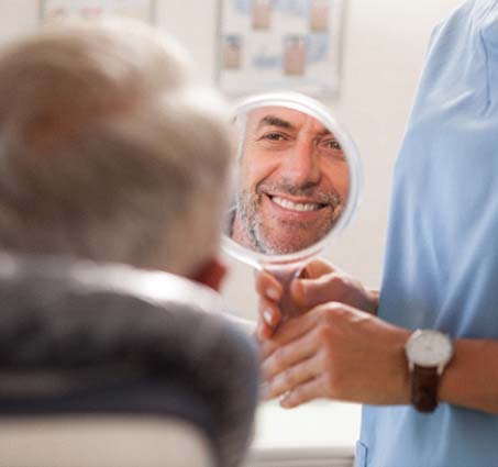 Man smiling in mirror after dental implant salvage in Flint, MI