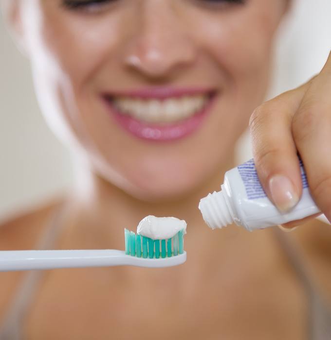 Patient placing toothpaste on toothbrush during dental hygiene routine