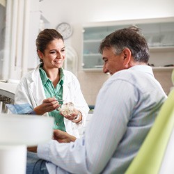 Smiling dentist showing patient model of teeth