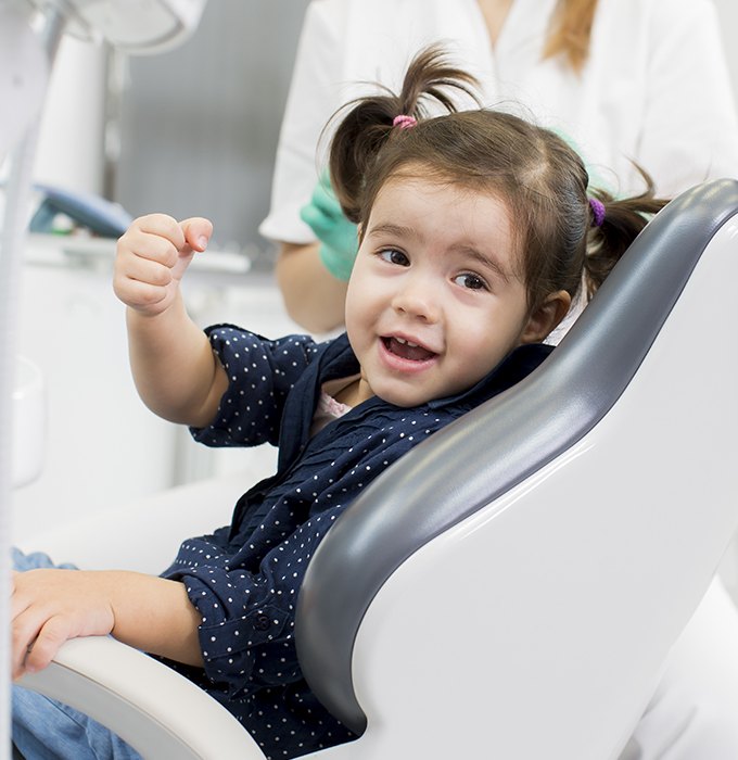 Little girl in dental chair for first visit smiling at dentist