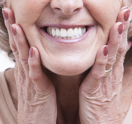 Senior woman touching her face and smiling with dentures in Flint