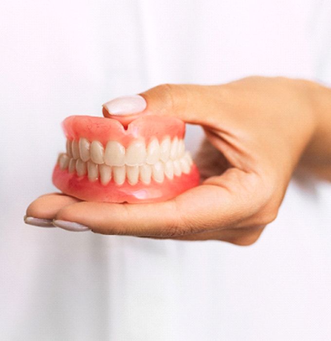 Closeup of person holding full dentures in Flint