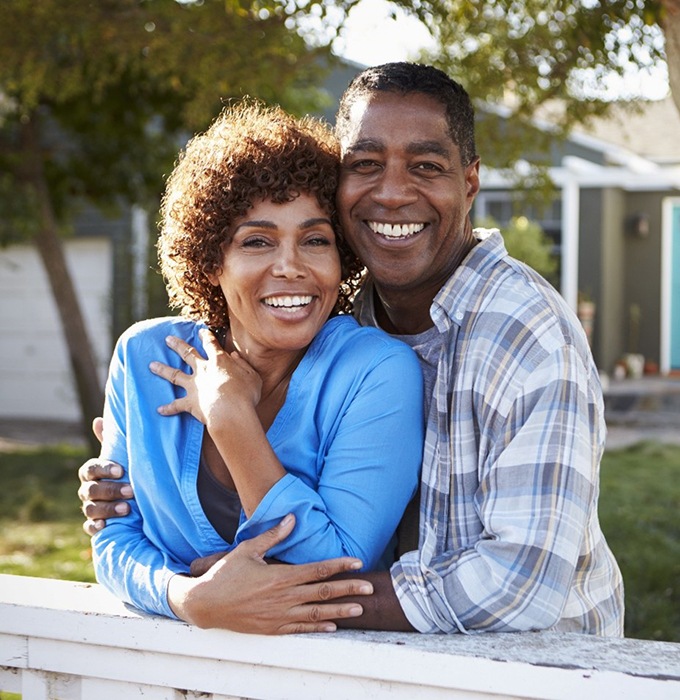 Smiling couple with dental implants in Flint standing outside 