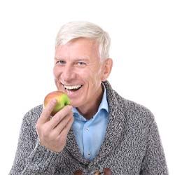 Older man in sweater biting into an apple