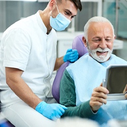 Patient using mirror to view smile with dentist in Flint