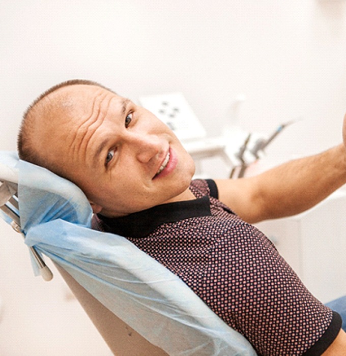 Man sitting back giving thumbs up after getting dental implants in Flint, MI