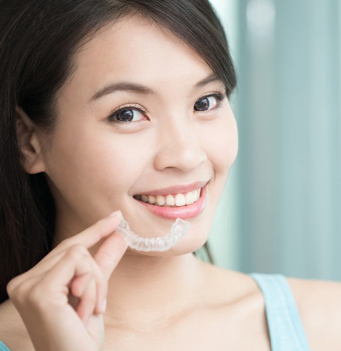 Smiling woman placing Invisalign clear braces tray