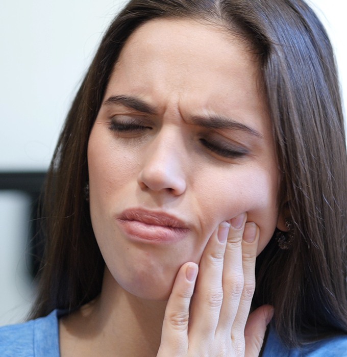 Woman in need of root canal therapy holding cheek in pain