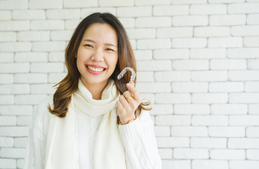 smiling woman in sweater holding Invisalign in Flint