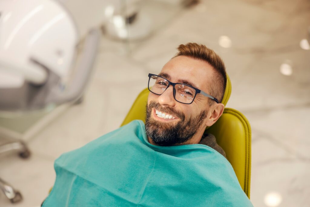 Man with glasses smiling while sitting in treatment chair