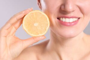 Nose-to-shoulder view of woman holding lemon next to her smile